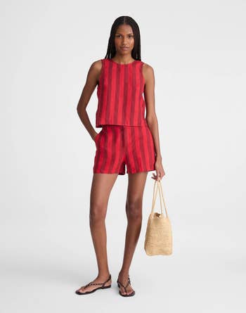 Person wearing a red striped tank and shorts set, standing with one hand on hip and holding a tote