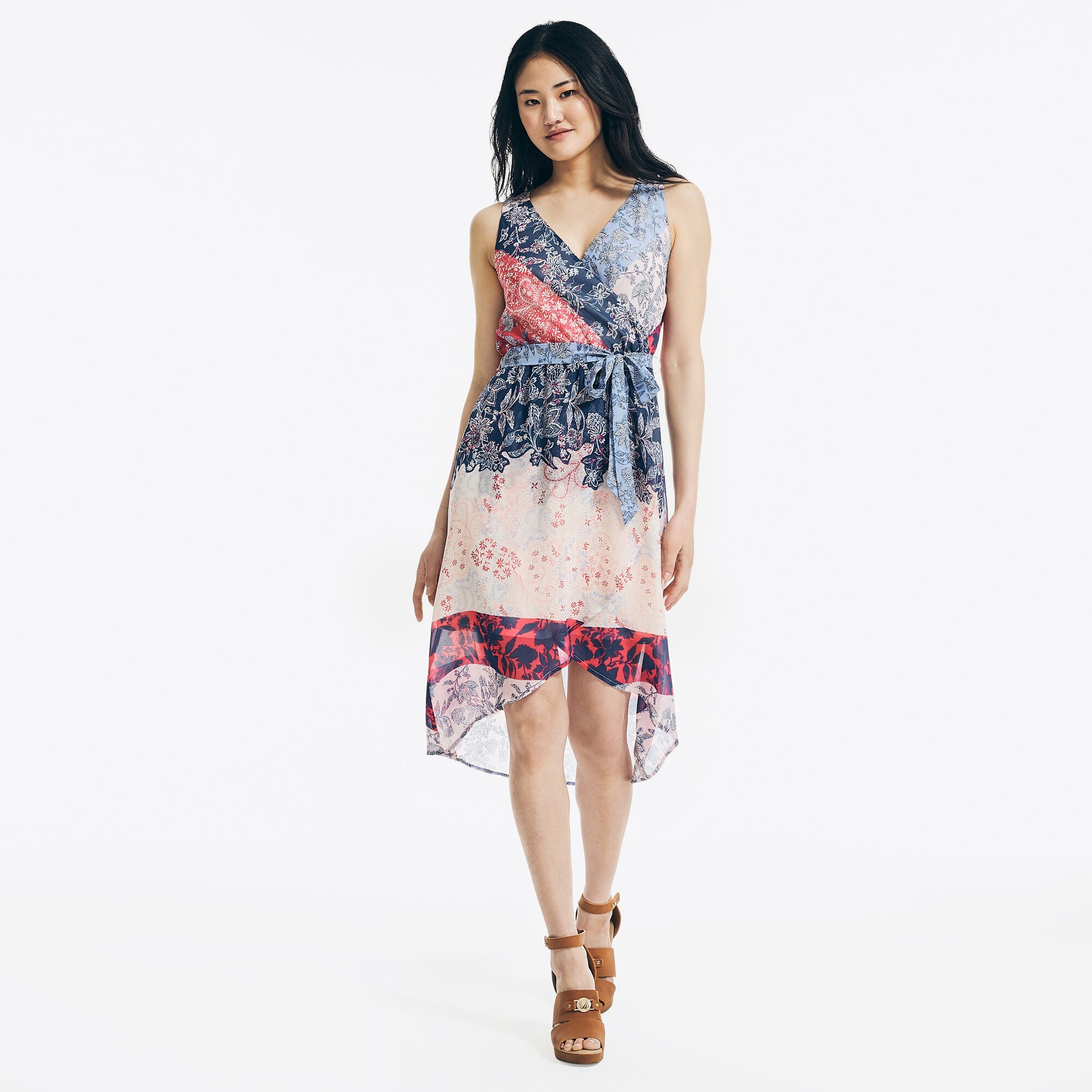 model in sleeveless wrap dress with sheer high-low hem that hits around the knees and has blue, red, and cream patterns