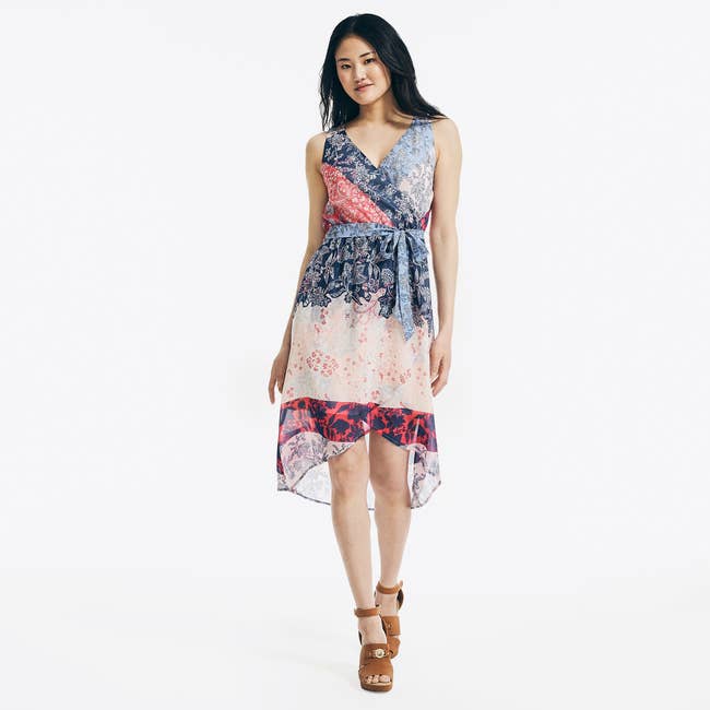 model in sleeveless wrap dress with sheer high-low hem that hits around the knees and has blue, red, and cream patterns