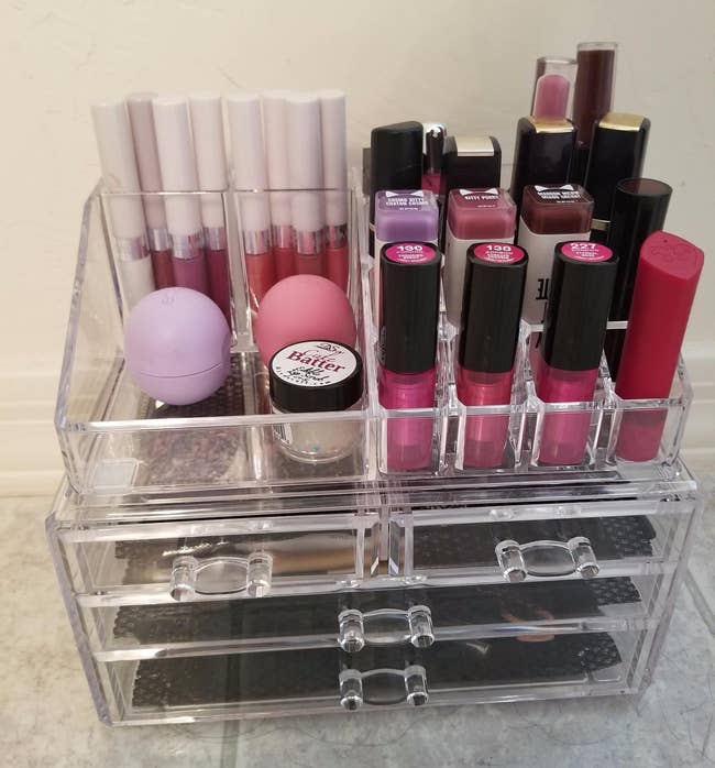 reviewer's clear makeup organizer filled with lipsticks on top and more beauty products in the drawers 