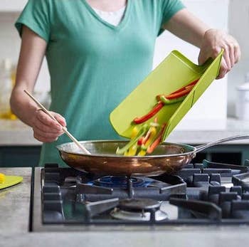 model pouring sliced peppers into a pan using the folded green cutting board