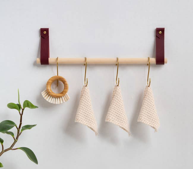 long dowel held up on a wall by two leather straps with four hooks with towels on them