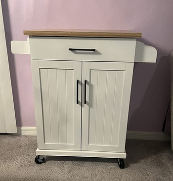 Reviewer image of white microwave cart with drawer and cabinet doors on carpet in front of purple wall