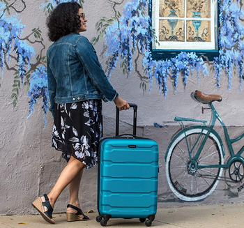 woman rolling a turquoise suitcase