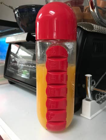 A clear water bottle with a red lid and a red pill box on the side 