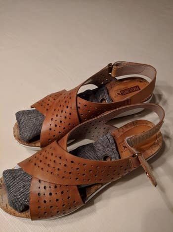 a reviewer's pair of brown perforated sandals with ankle straps on a table, suitable for a shopping article on summer footwear