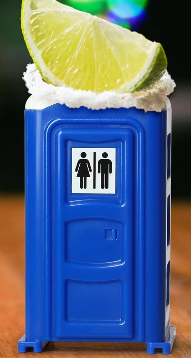 Toy portable toilet with whipped cream and a lime wedge on top, resembling a quirky cocktail presentation