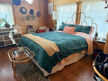 Cozy chamber with a woody interior, featuring a furniture with greenish bedding and decorative pillows, a tiny circular table, and earthy airy from windows