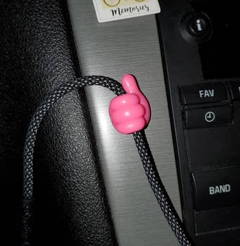 reviewer image of the pink thumbs up cord organizer holding a cord in a car