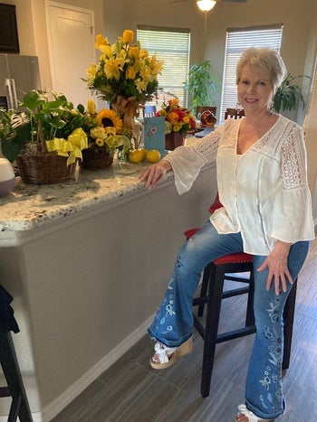 reviewer wearing light blue flare jeans with embroidered roses, sitting at a kitchen stool
