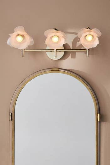 the lit sconce above a mirror with three blossoms