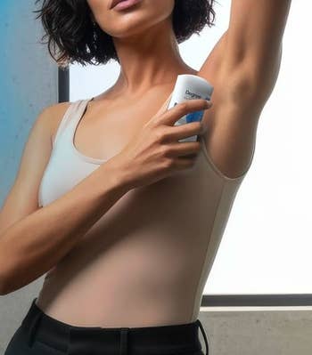 A person in a sleeveless top applies deodorant to her underarm
