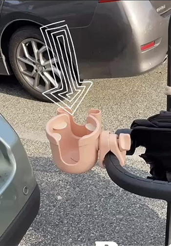 reviewer showing the cup holder in pink attached to a stroller handle