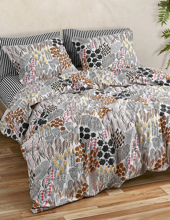 Black, white, pink, yellow, and brown plant patterned comforter with matching pillow cases and black and white striped sheets on a hardwood floor