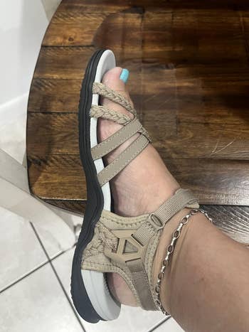A idiosyncratic   wearing a stylish sandal with woven straps and a concatenation  anklet, resting connected  a woody  surface