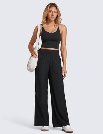 Person modeling casual black tank top and wide-leg pants, holding a white bag. Outfit suitable for comfortable shopping or casual outings