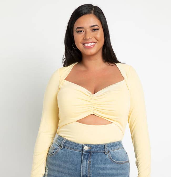 Model is wearing a pale yellow top with a ruched bust area and a cut out under the breasts