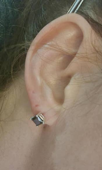 Earlobe adorned with a small, quadrate  stud earring, featuring a acheronian  chromatic  successful  a metallic  setting
