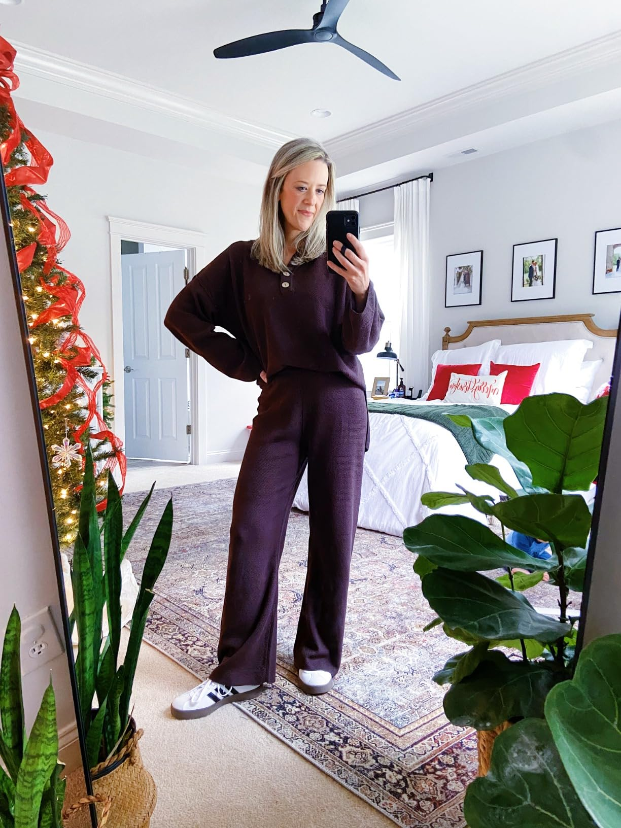Woman in comfy loungewear takes a mirror selfie in a stylish bedroom with holiday decor and plants