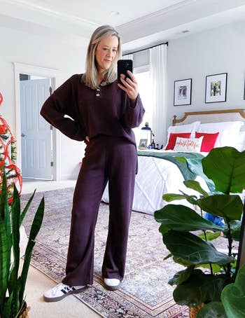 Woman in comfy loungewear takes a mirror selfie in a stylish bedroom with holiday decor and plants