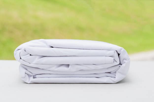 A neatly folded white bedsheet placed on a light surface with a blurred green background