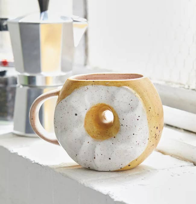 A mug with a hole in the middle painted like an everythign bagel with cream cheese 