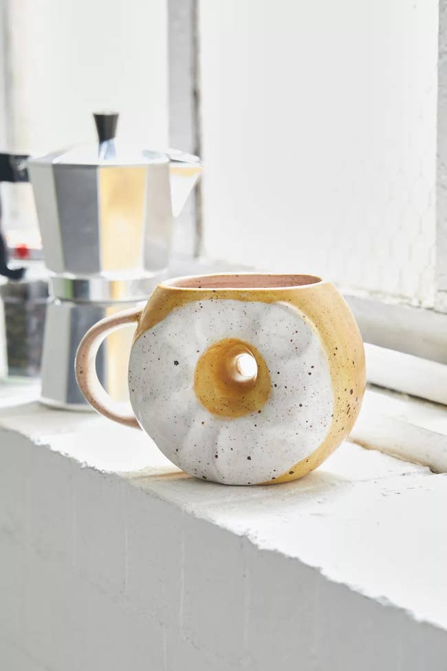 A mug with a hole in the middle painted like an everythign bagel with cream cheese 