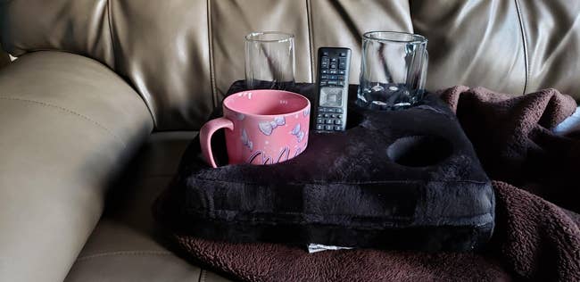 A couch cushion cupholder holding a mug, two glasses, and a remote
