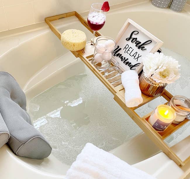 reviewer photo of the bathtub tray holding a candle, glass of wine, and bath products