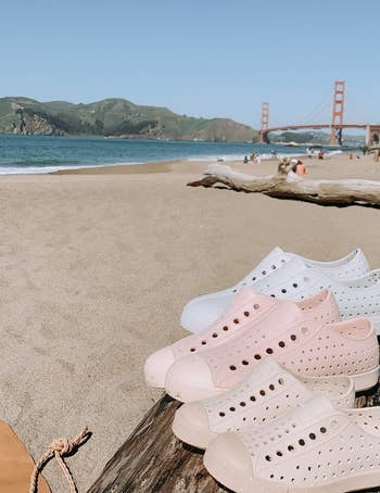 multiple jefferson bloom sneakers sitting on a log on a beach, in three shades: white, light pink, and beige