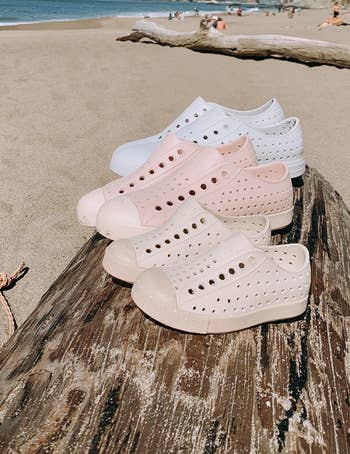 multiple jefferson bloom sneakers sitting on a log on a beach, in three shades: white, light pink, and beige