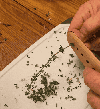 gif of someone feeding an herb sprig through a hole in the herb stripper to remove the leaves from the stem