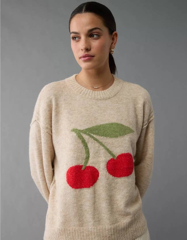 Person wearing a sweater with a cherry design, looking to the side. Styled for a casual, chic look, suitable for a Shopping article