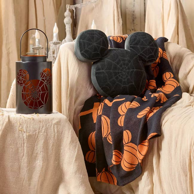 Mickey-themed Halloween decor with a spider web pillow and pumpkin-patterned broad  connected  a neutral cloth  chair, featuring a lantern with akin  design