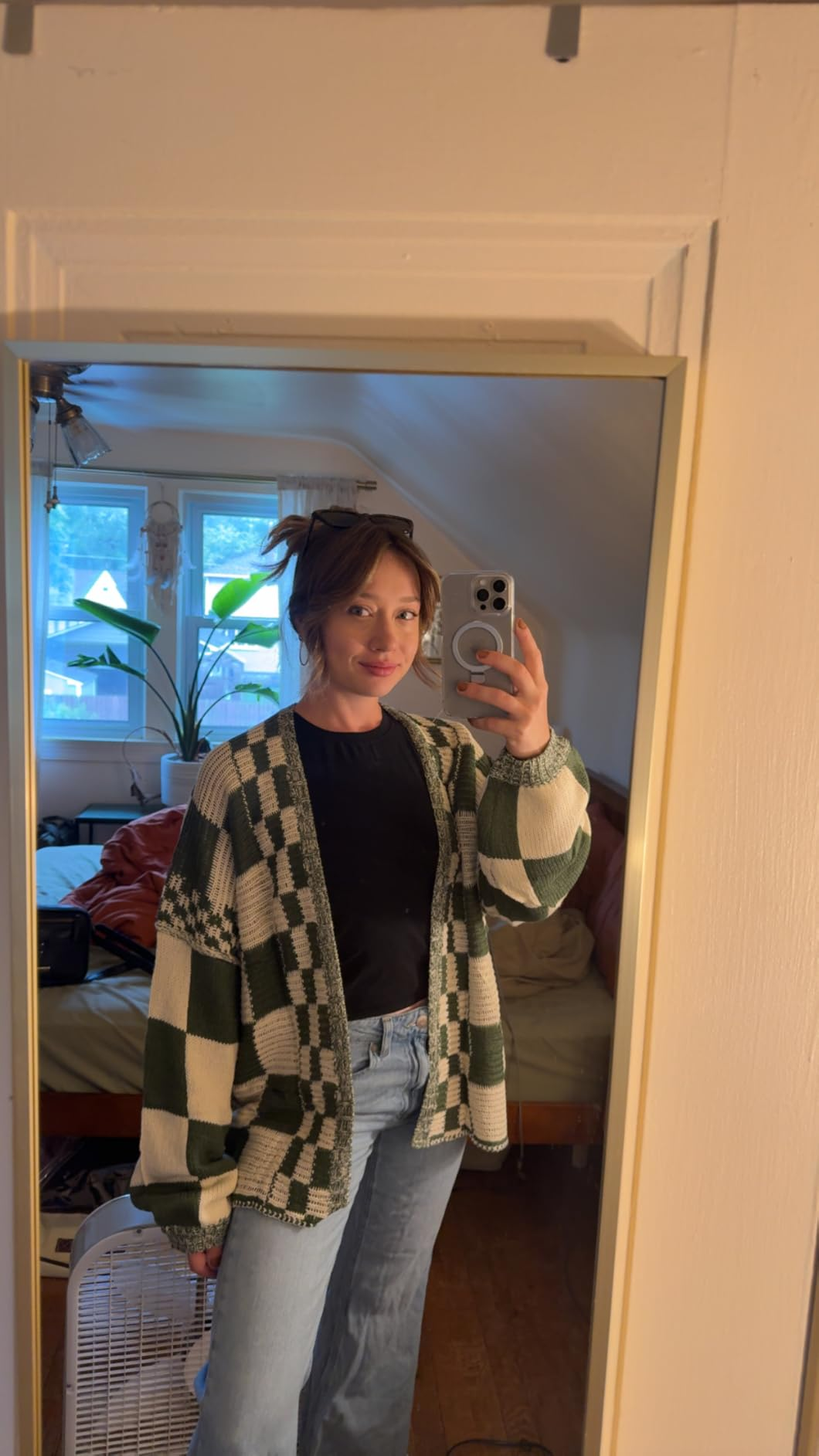 Person successful  a reflector  selfie wears a checkered cardigan, achromatic  shirt, and jeans, lasting  successful  a cozy bedroom