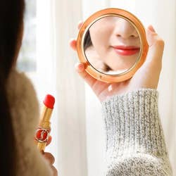 model using the macaron as a mirror while applying lipstick