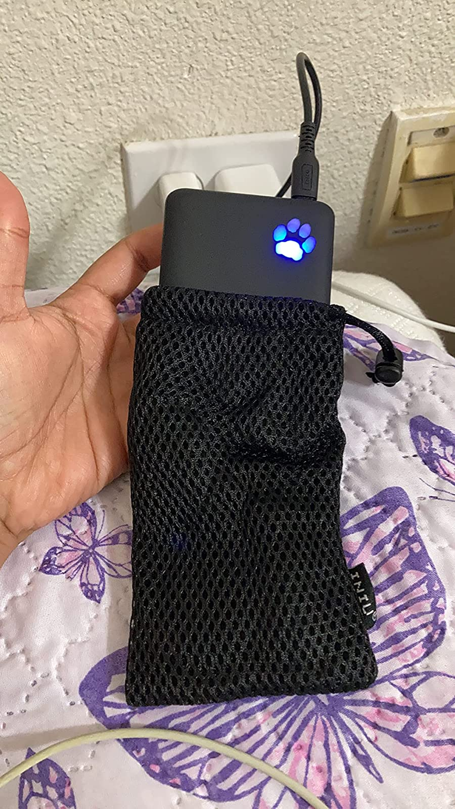 a hand holding up the power bank while it's halfway in its mesh carrying bag