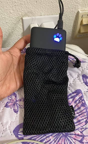 a hand holding up the power bank while it's halfway in its mesh carrying bag