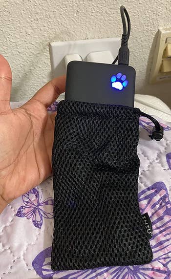 a hand holding up the power bank while it's halfway in its mesh carrying bag
