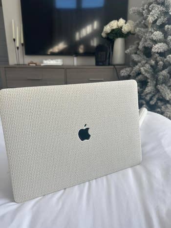 A laptop with a textured cover featuring an Apple logo is placed on a bed.