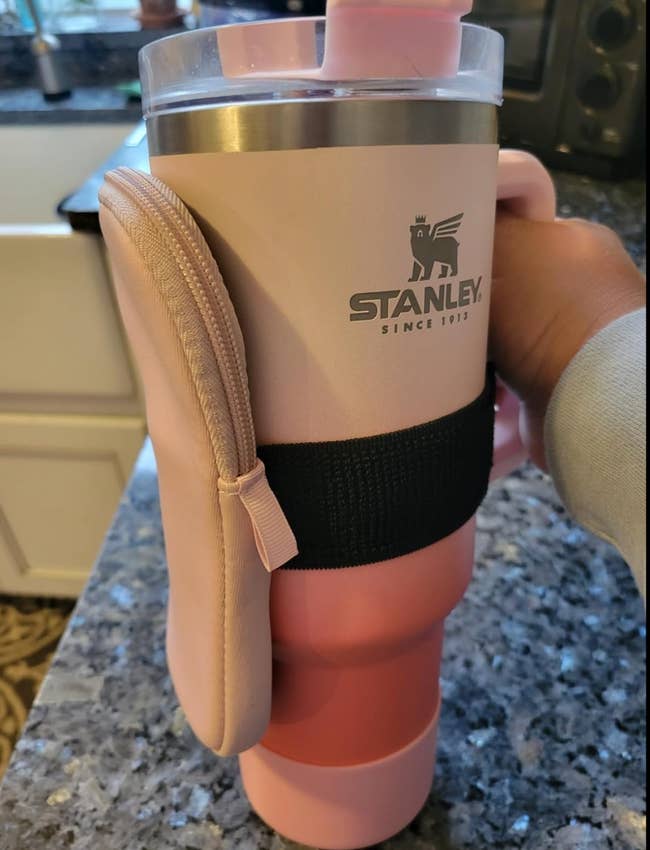 Person holding a pink Stanley travel mug with a handle strap attached to a pink pouch 