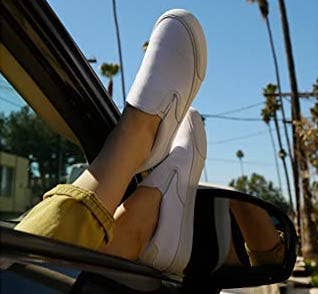model's feet hanging out a car window and wearing the white slip ons