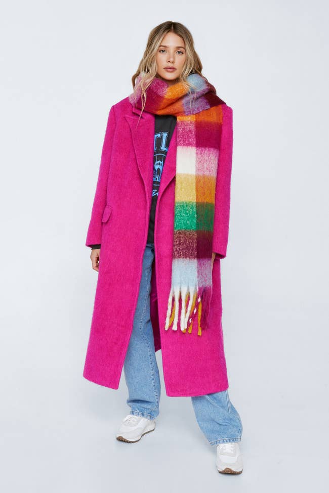 a model posing in the pink coat with a plaid scarf and blue jeans