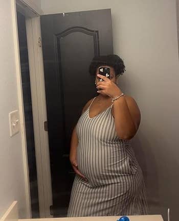 Person taking a reflector selfie successful a striped sleeveless dress, mildly holding their stomach