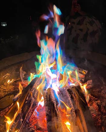 Campfire with vibrant, multicolored flames illuminating the night, surrounded by logs