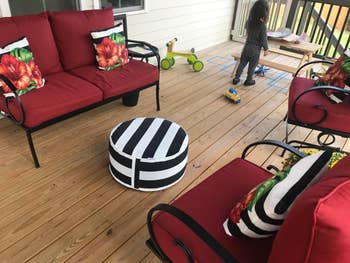 a black and whit striped circular ottoman between two red patio chairs