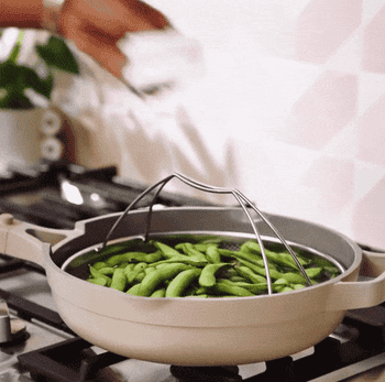 gif of someone lifting a metal steaming basket filled with edamame out of the taupe always pan