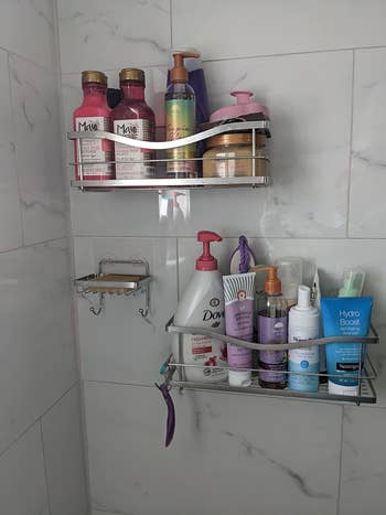 A different reviewer image of silver shelves attached to a shower wall with lots of products in them 