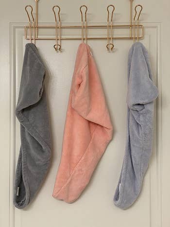 reviewer photo of three microfiber towel wraps in gray, pink, and blue hanging on the back of a door