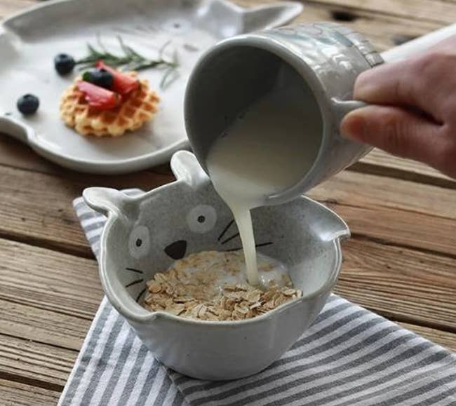 The Totoro bowl with oatmeal inside while someone pours milk inside
